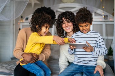 Mutlu çoklu etnik aile dijital cihazlarla eğleniyor. Homoseksüel ebeveynler ve küçük çocuklar dijital tablet kullanıyorlar..