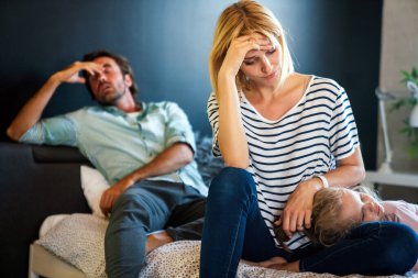 Tired young mother and father sitting on couch feels annoyed exhausted stressful with little girl child.