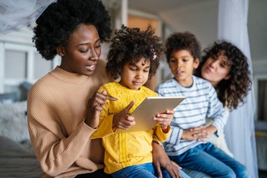 Mutlu çoklu etnik aile dijital cihazlarla eğleniyor. Homoseksüel ebeveynler ve küçük çocuklar dijital tablet kullanıyorlar..