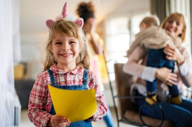 Bekar annesi ve kardeşleri arka planda oynarken gülümseyen mutlu küçük bir kızın portresi.