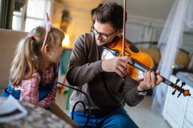 Müzik çok eğlenceli. Genç baba küçük kızına keman çalmayı öğretiyor ve gülümsüyor. Ebeveyn çocuk mutluluğu kavramı.