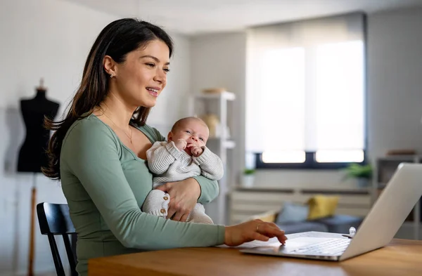 Stay at home mom working remotely on laptop while taking care of her baby. Young mother on maternity leave trying to freelance by the desk with child