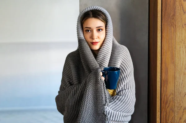Freezing woman covered with a cozy blanket. Female wrapped in warm blanket, drinking hot drink. Cold flu concept.