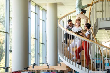 Eğitim kampüsü arkadaşlığı ve insanların konsepti. Bir grup mutlu öğrenci kütüphanede birlikte okuyorlar..