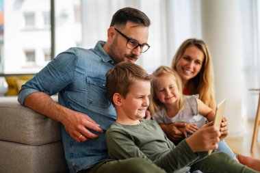 Mutlu genç aile evde eğleniyor. Çocuklu aileler dijital cihaz kullanıyor. Eğitim ebeveynliği mutluluk kavramı.