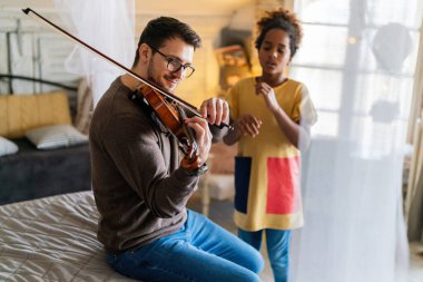 Müzik çok eğlenceli. Genç baba küçük kızına keman çalmayı öğretiyor ve gülümsüyor. Ebeveyn çocuk mutluluğu kavramı.