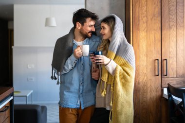 Sıcak içeceklerle evde sıcak battaniyenin altında sarılan mutlu genç çift. Hafta sonu insanları aşk kavramını rahatlatır.