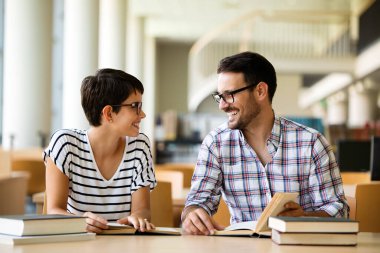 Mutlu genç üniversite öğrencileri ile kütüphane kitaplarında. Bir grup üniversite kitaplığında çok ırklı insan.