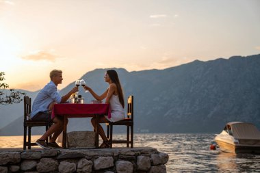 Aşık bir çift plajda gün batımında romantik bir akşam yemeğinde şarap içiyor. Genç çift yıldönümü, doğum günü, Sevgililer Günü 'nü kutluyor..