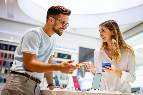 Genç ve tatmin olmuş bir çift, teknoloji mağazasının masasındaki cep telefonunun yeni modelini test ediyor..