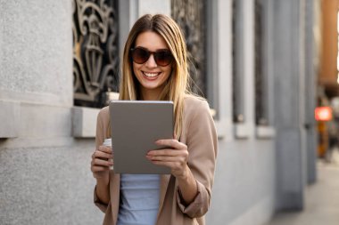 Dijital tablet kullanan başarılı bir genç kadının portresi kentsel arkaplanda kısa bir mola sırasında