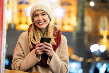 Alışveriş yapan kadın Noel 'de sokakta akıllı telefondan internetten alışveriş yapıyor. İnsanlar alışveriş teknolojisi konsepti