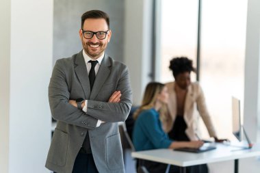 Handsome young successful business man standing confident in the corporate office in front of his team clipart