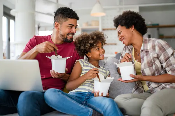 stock image Lunch at home with fast food takeaway restaurant. Happy african american family eating on couch with cardboard boxes in living room interior