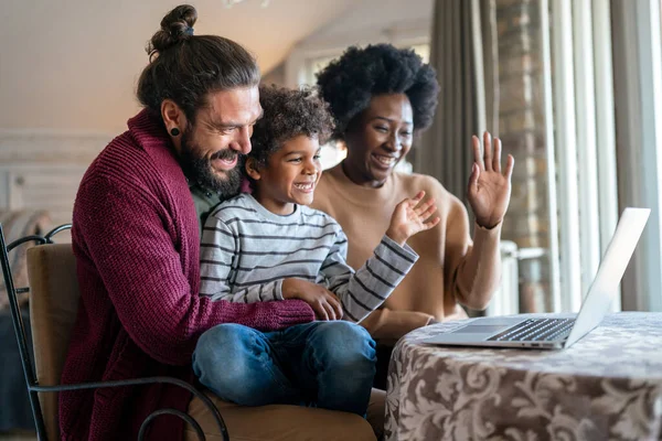 Happy diverse multiethnic family gathering around laptop and having fun during a video call at home. Multi ethnic parents enjoying quality time with child while using digital device.