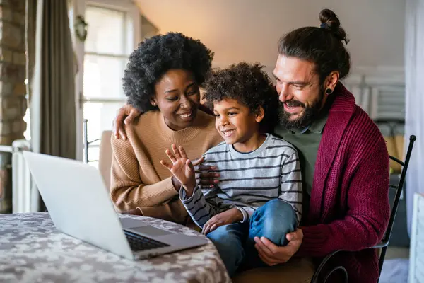 Diverse family waving during a video call at home. Happy ethnic family smiling cheerfully while greeting their loved ones using a digital tablet. Parents spending time with their child at home.