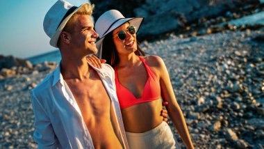 Kumsalda yürüyen bir çift. Genç mutlu insanlar kumsalda yürüyor gülümsüyor, yaz tatilinin tadını çıkarıyor.