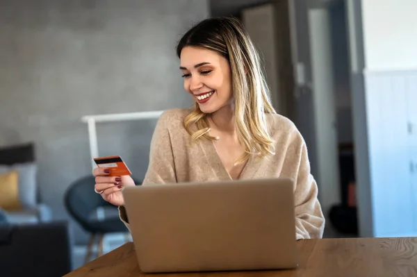 Beautiful woman with laptop and credit card at home, portrait. Young businesswoman using a computer while holding a credit card in an home office