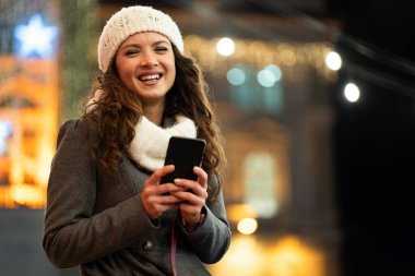 Kışın sokakta cep telefonu kullanan mutlu güzel bir kadın. Noel iletişimi insanları kavramı