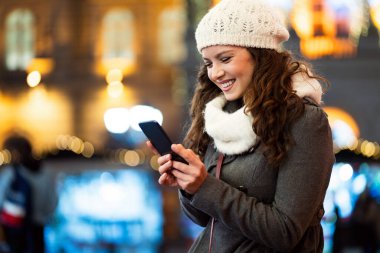 Kışın sokakta cep telefonu kullanan mutlu güzel bir kadın. Noel iletişimi insanları kavramı