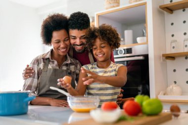 Coşkulu Afro-Amerikalı çocuklu genç bir aile evde birlikte yemek pişiriyor, mutlu gülümseyen ebeveynler hafta sonları mutfakta çocukla eğleniyor.