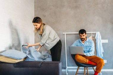 Genç kadın temizlik yaparken erkek ev bilgisayarında çalışıyor. Evden çalışma, sosyal medya kavramı.