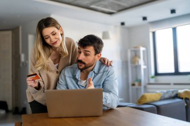 Evde dizüstü bilgisayarlarındaki banka hesaplarına bakarken tartışan hoşnutsuz genç bir çift. Çevrimiçi alışveriş kavramı.