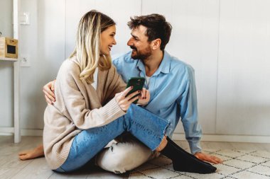 Akıllı telefona bakarken kucaklaşan gülümseyen genç çift. Sosyal medyayı akıllı telefondan paylaşan çok ırklı çift.