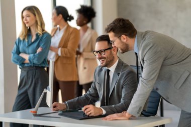 Ofiste yeni bir proje üzerinde çalışırken gülen iş adamları. Modern bir çalışma alanında çalışırken bilgisayar kullanan bir grup farklı iş adamı..