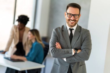 Yakışıklı, başarılı bir iş adamı ekibinin önünde şirket ofisinde kendinden emin duruyor.