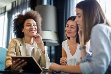 Kadın ve müşterileri iş görüşlerini tartışıyor ve bir kafede kahve içerken işbirliği yapıyorlar. Mutlu iş ortakları bir öğle yemeği toplantısında birbirleriyle iletişim kurarken dijital bir cihaz kullanıyorlar..