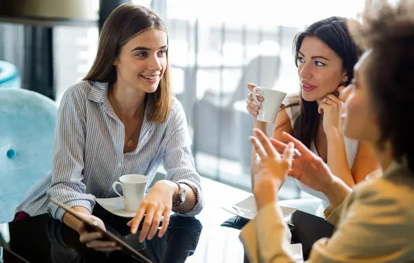 Woman and her clients discuss business ideas and collaborate over coffee in a cafe. Happy business partners using a digital device as they engage with each other in a lunch meeting.