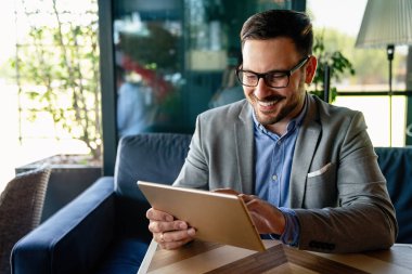 Gülümseyen başarılı iş adamı, resmi iş süitinde dijital tablet üzerinde çalışan girişimci