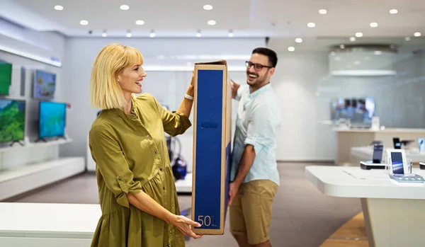 Cheerful young couple carrying packed TV they bought on sale. Tech store interior concept