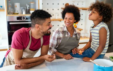 Mutlu Afro-Amerikan gülümseyen ailesi mutfakta sağlıklı yemekler hazırlıyor, hafta sonları birlikte eğleniyorlar.