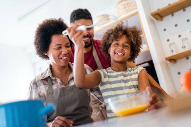 Coşkulu Afro-Amerikalı çocuklu genç bir aile evde birlikte yemek pişiriyor, mutlu gülümseyen ebeveynler hafta sonları mutfakta çocukla eğleniyor.