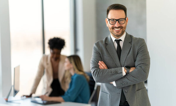 Young happy successful young businessman with arms crossed smiling at corporate office