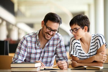 Kütüphanede kitaplarla çalışan mutlu genç üniversite öğrencileri. Üniversitede bir grup çok ırklı insan