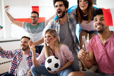 Genç, mutlu bir arkadaş grubu televizyonda spor izliyor ve tezahürat yapıyor.