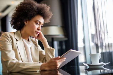 Çekici genç başarı Afro-Amerikan iş kadını kahve içiyor ve bir mola sırasında dijital tablet kullanıyor.