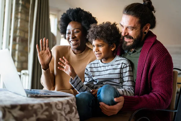 Happy diverse multiethnic family gathering around laptop and having fun during a video call at home. Multi ethnic parents enjoying quality time with child while using digital device.