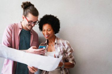 Ofiste yeni bir proje üzerinde çalışırken gülen iş adamları. Modern bir çalışma alanında birlikte çalışırken, çeşitli iş adamlarından oluşan bir grup plan kullanıyor..