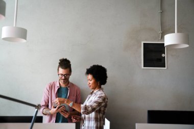 İki iş adamı dijital tablet bilgisayarı kullanarak birlikte çalışıyor ve bir iş projesi hakkında konuşuyorlar. Yöneticilerden oluşan küçük yaratıcı çeşitlilik ekibi ofiste çalışıyor..