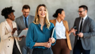 Arka planda çok ırklı meslektaşlar çalışırken başarılı iş kadını ve girişimcinin portresi.