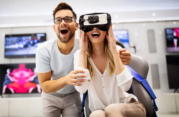 Young happy couple playing video games with virtual reality glasses in technical store. Cheerful people having fun with new trends technology