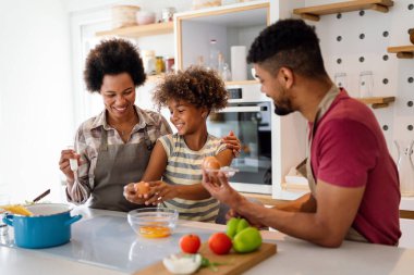 Coşkulu Afro-Amerikalı çocuklu genç bir aile evde birlikte yemek pişiriyor, mutlu gülümseyen ebeveynler hafta sonları mutfakta çocukla eğleniyor.