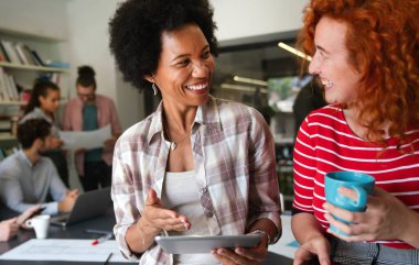 Dijital tablet bilgisayar kullanarak birlikte çalışan iki iş kadını bir iş projesi hakkında konuşuyor. Kadın yöneticilerden oluşan küçük yaratıcı çeşitlilik ekibi ofiste çalışıyor..