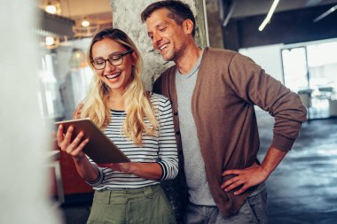 Çeşitli meslektaşları tablet kullanarak çevrimiçi projeyi tartışarak kapat. Gülümseyen iş kadını ve işadamı cihaz ekranına bakıyor, ofiste birlikte çalışıyorlar.