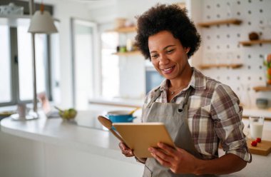 Genç Afrikalı Amerikalı kadın mutfağında yemek pişirmek için tablet bilgisayar kullanıyor. İnsanlar teknoloji gıda kavramı.