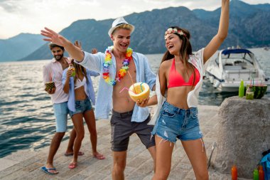 Plaj partisinde tropikal kokteyllerle eğlenen mutlu genç arkadaşlar. Seyahat ve yaz tatili konsepti.